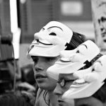 Demonstrators with masks at a demonstration in support of Assange, his photo faintly visible on a sign in the background.