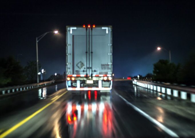 Viewed from behind: A semi driving down the highway at night.