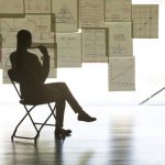Business person sitting on a folding chair looking at a wall hung with charts and graphs.
