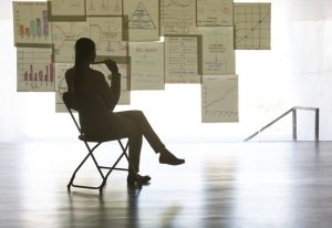 Business person sitting on a folding chair, contemplating a wall full of charts and graphs.