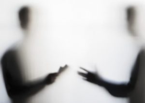 Two symmetical shadowy male figures, out of focus, facing each other and gesturing as if talking to each other.