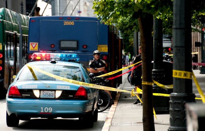 Crime scene, police car and paddy wagon in the street; yellow tape around an area of the sidewalk.