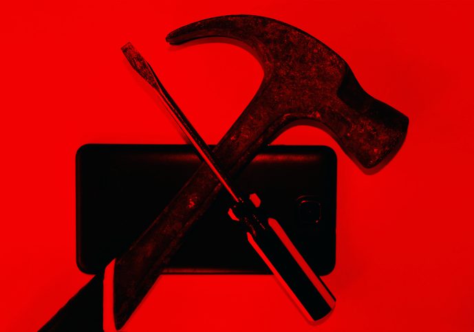 Ominous looking objects in silhouette - screw driver and hammer crossed in front of a cellphone.