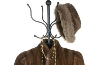 Fur coat, gold necklace and fancy possibly men's fur hat, hanging on a coat rack.