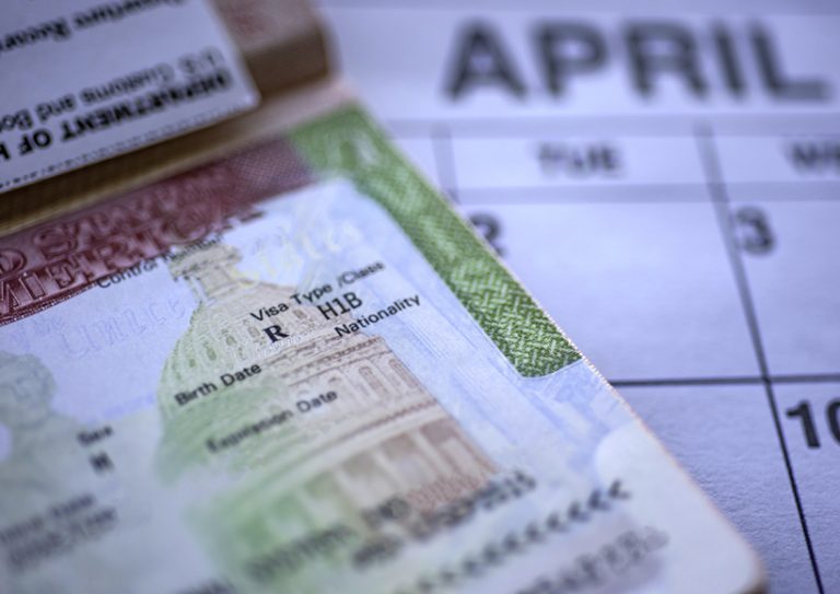 H1B visa (for specialty workers) stamp in passport, blurred april calendar on background. H1B visa program deadline concept. Close up view. H1B visa for specialty workers