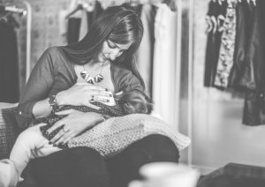 Black & white photo of a nursing mother sitting comfortably in what looks like it could be storage closet.