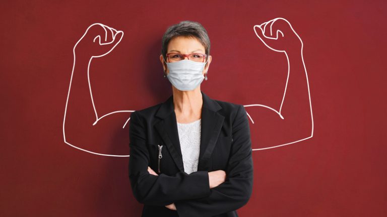 Woman wearing mask facing forward, arms folded. The background is a superimposed sketch of a muscular arms flexing biceps.