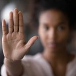 Woman looking at viewer. Her face is somewhat blurry, but here hand is in focus, held up palm forward, as if to say "no."