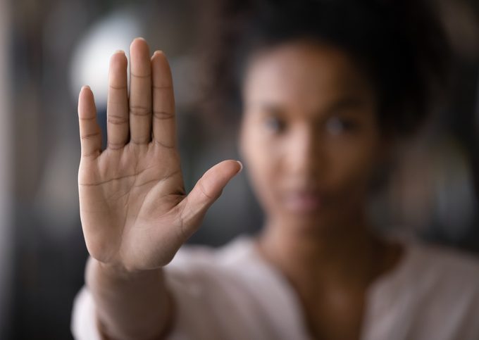 Close up of ethnic woman show palm demonstrate protest Woman looking at viewer. Her face is somewhat blurry, but here hand is in focus, held up palm forward, as if to say "no."