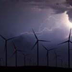 A field of wind turbines at night in a storm, lit up by lightening.