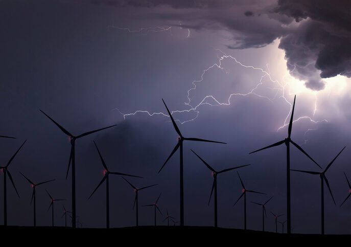 A field of wind turbines at night in a storm, lit up by lightening.