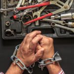 Shackled hands before a collection of tools in open container.