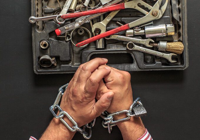Right to repair Shackled hands before a collection of tools in open container.