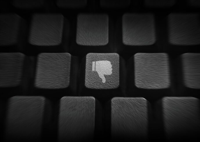 thumb down or dislike button on keyboard. Keyboard in shadows, with a white "thumbs down" image on one of the keys.