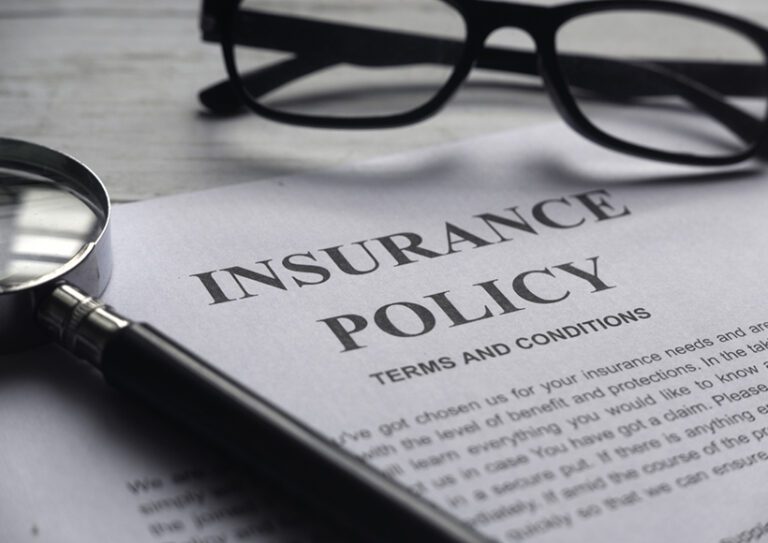 Selective focus of magnifying glass,glasses and Insurance Policy letter on a white wooden background. insurance policy