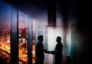 businessmen-shaking-hands-in-office-at-night-with-city-view-picture-id637945960